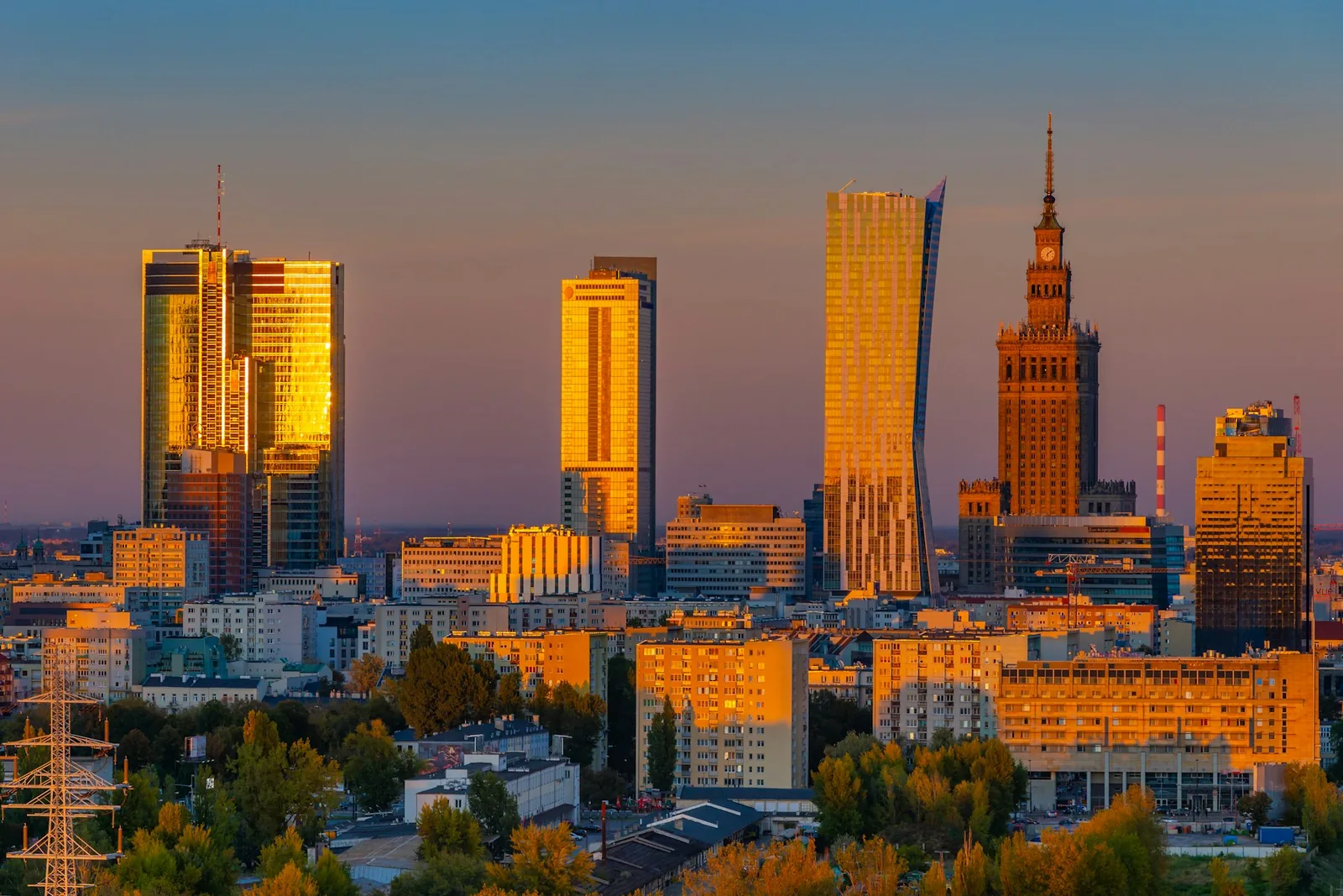Warsaw’s skyline in golden evening sunlight, with Złota 44 and the Palace of Culture and Science beneath a clear sky.