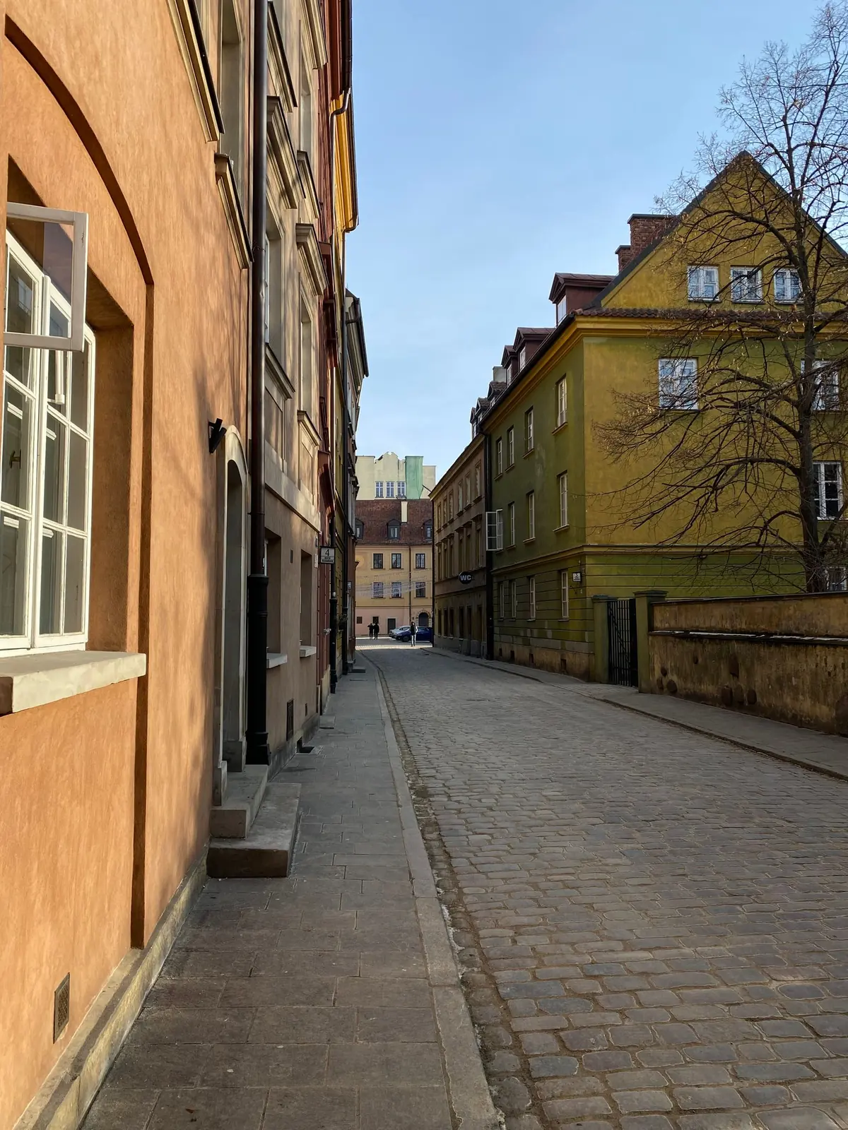 Warm façades and a cobbled street in Warsaw’s Old Town beneath a clear blue sky.